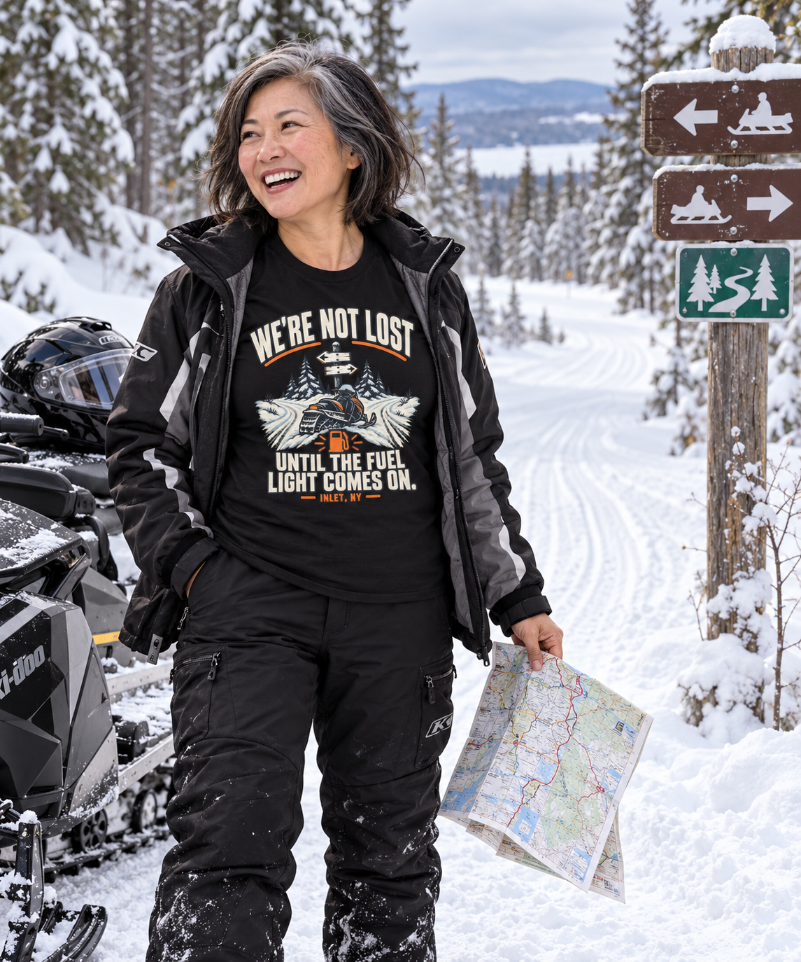 Woman checking a trail map beside a snowmobile in Inlet wearing the We're Not Lost tee
