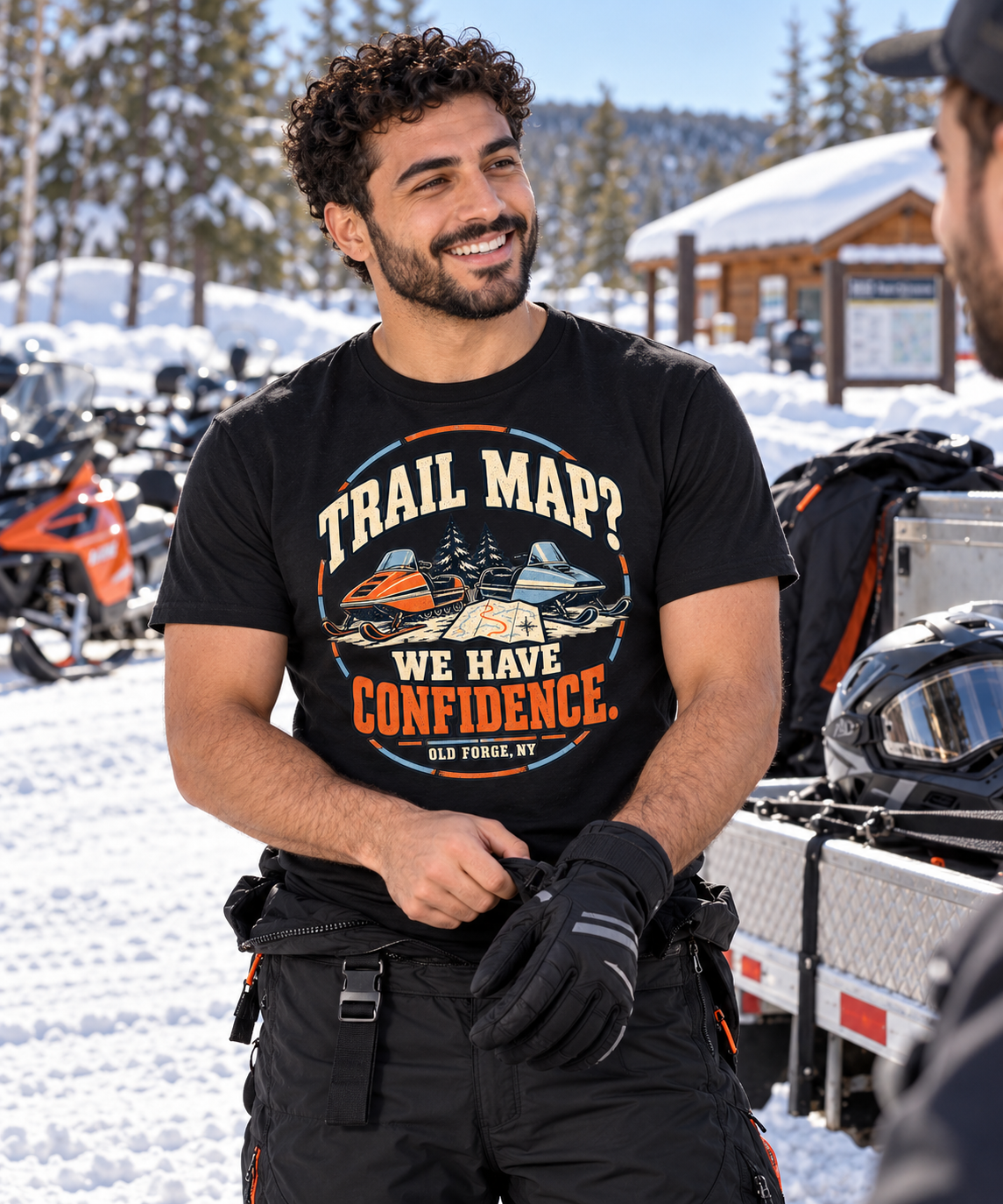 Rider pulling on gloves beside a snowmobile trailer wearing the Trail Map We Have Confidence tee