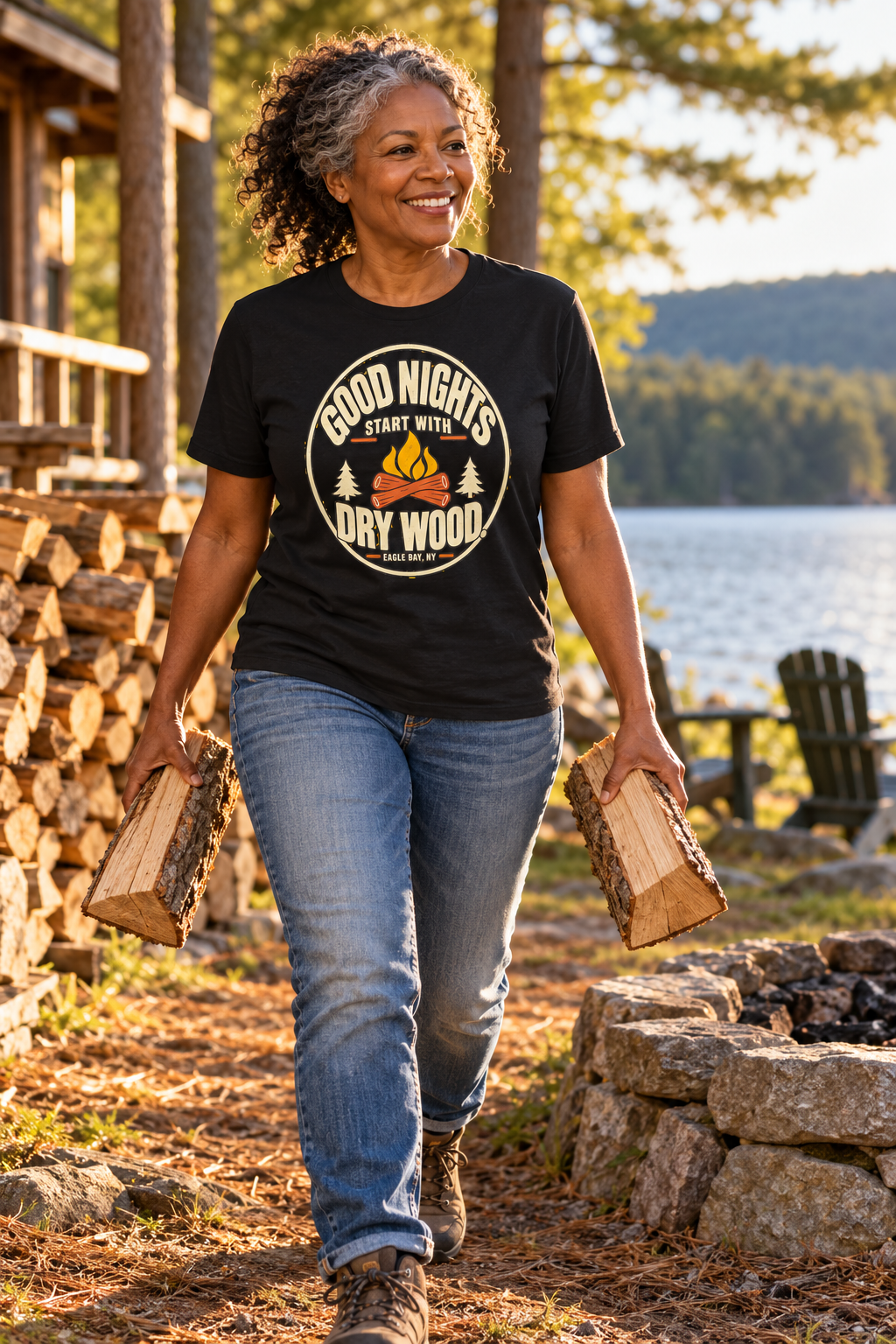 Woman carrying split firewood at lakeside camp wearing the Eagle Bay Good Nights Start With Dry Wood tee