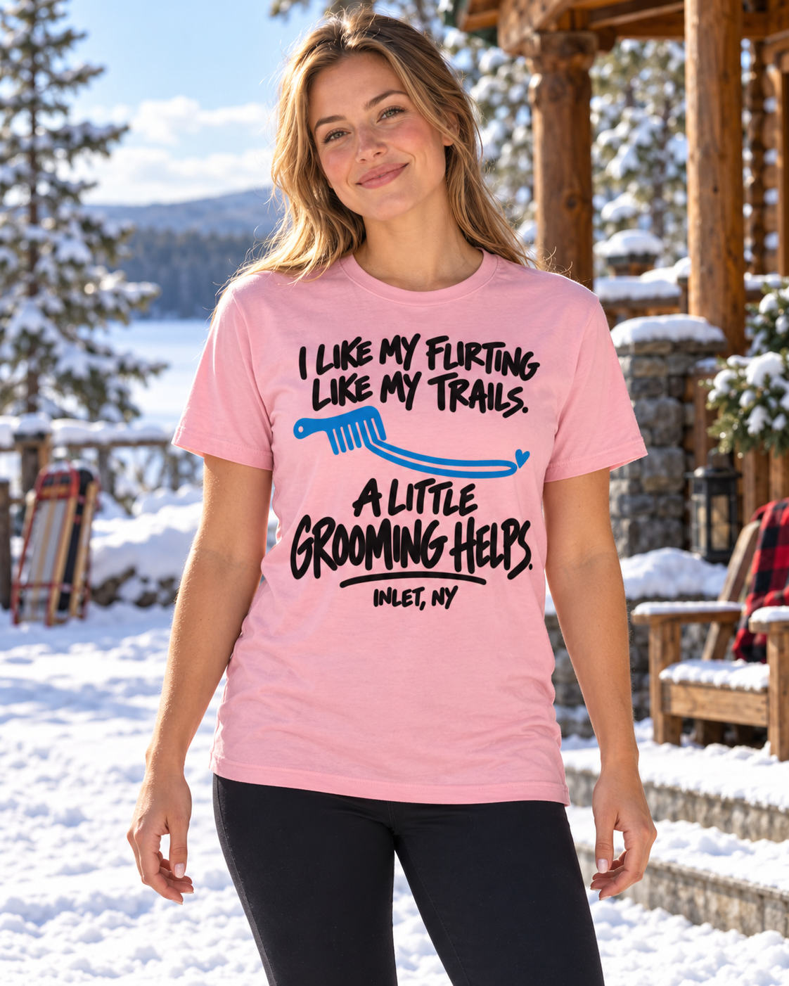 Woman wearing pink Inlet Snow Angels A Little Grooming Helps tee outside a snowy Adirondack cabin