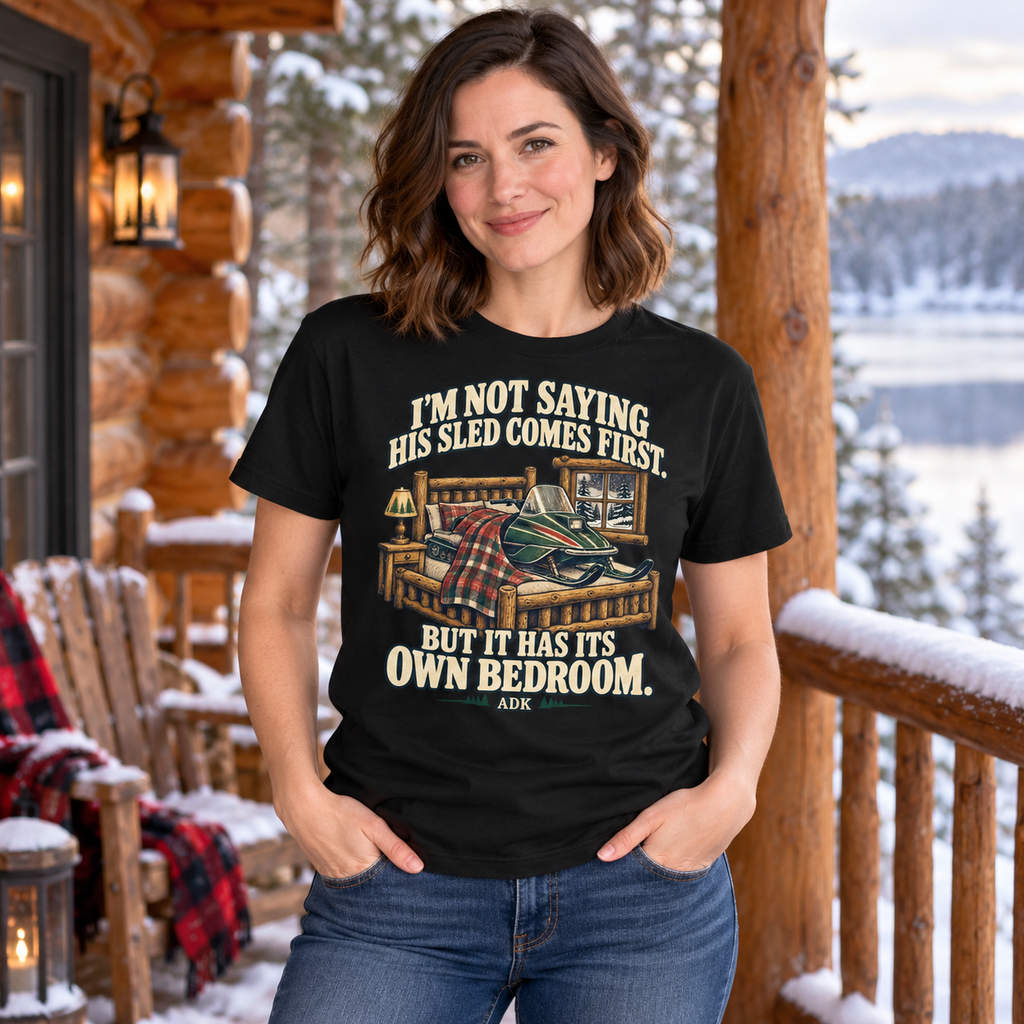 Woman wearing His Sled Has Its Own Bedroom tee on a snowy Adirondack cabin porch