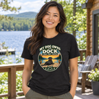 AI-generated lifestyle mockup of a woman wearing the black heather My Dog Owns the Dock tee beside a lake.